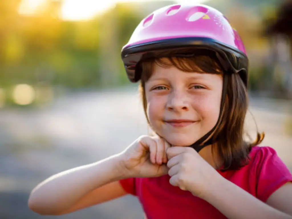a young kid is trying wear on her pink helmet